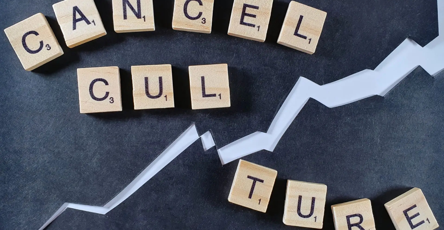 Scrabble-Steine, die das Wort Cancel Culture auf schwarzer Pappe legen.