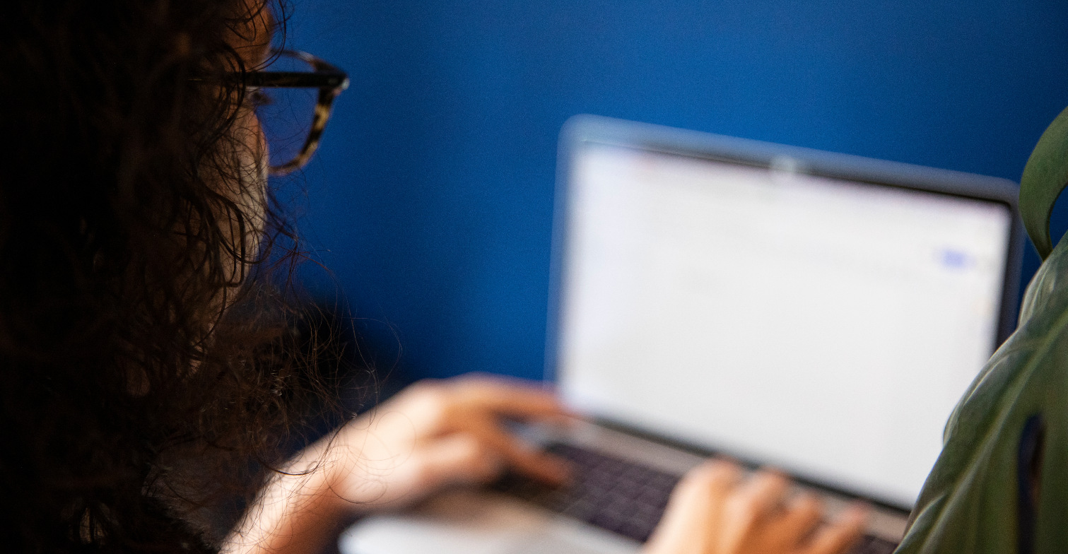 Eine Frau arbeitet an einem Laptop, sie ist von hinten fotografiert.