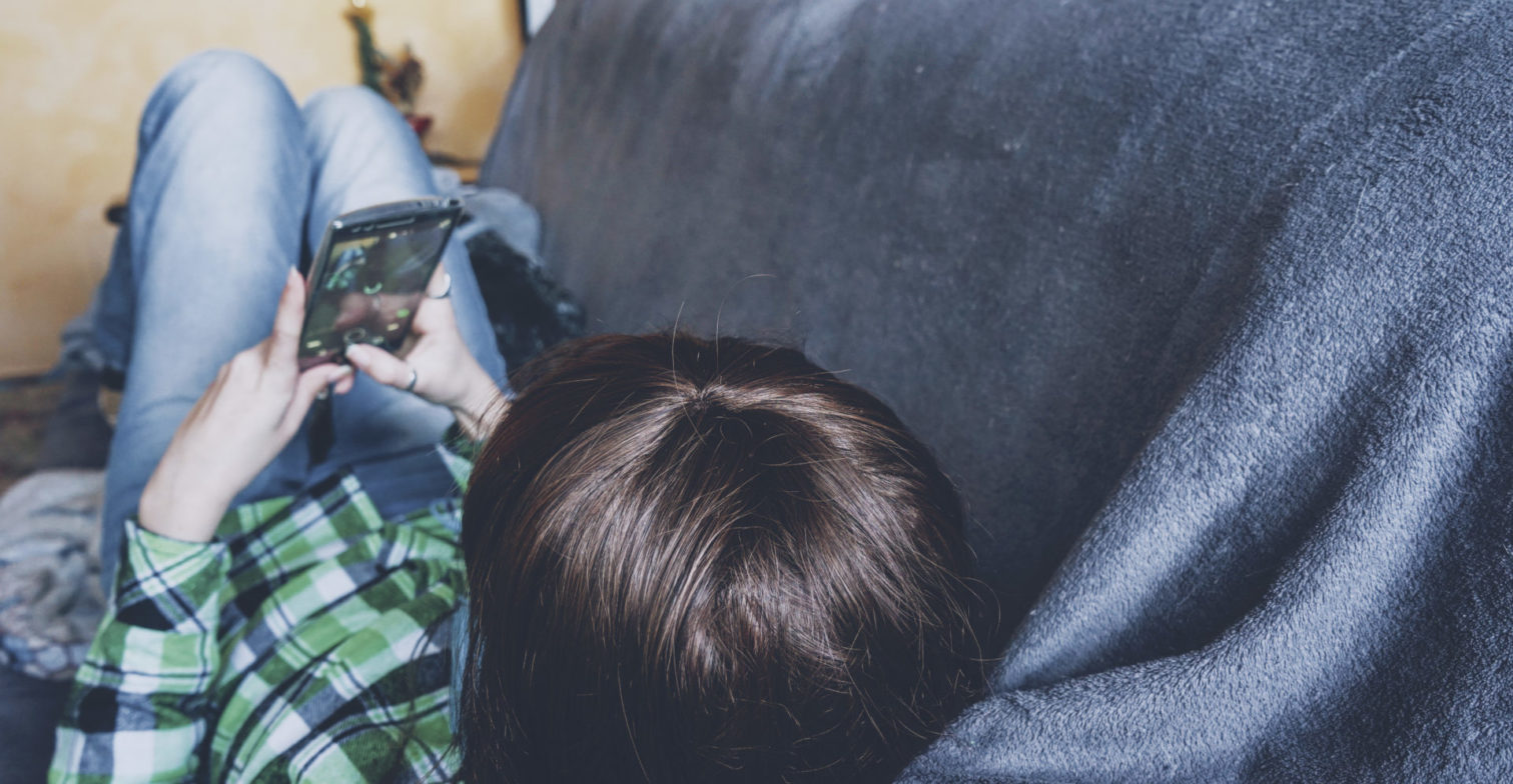 Junge Person liegt auf dem Sofa und schreibt auf dem Handy.