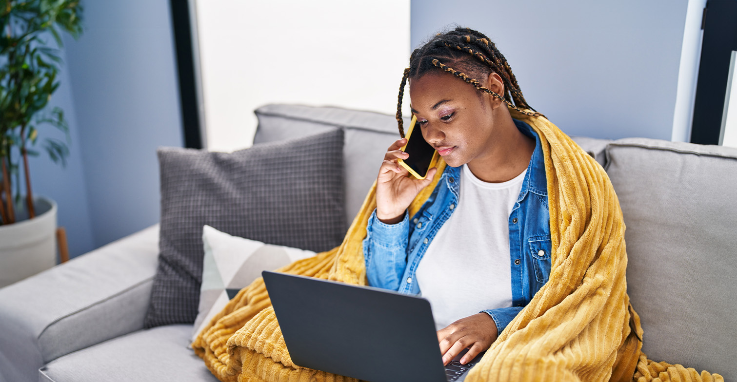 BIPoC telefoniert und schaut auf einen Laptop.