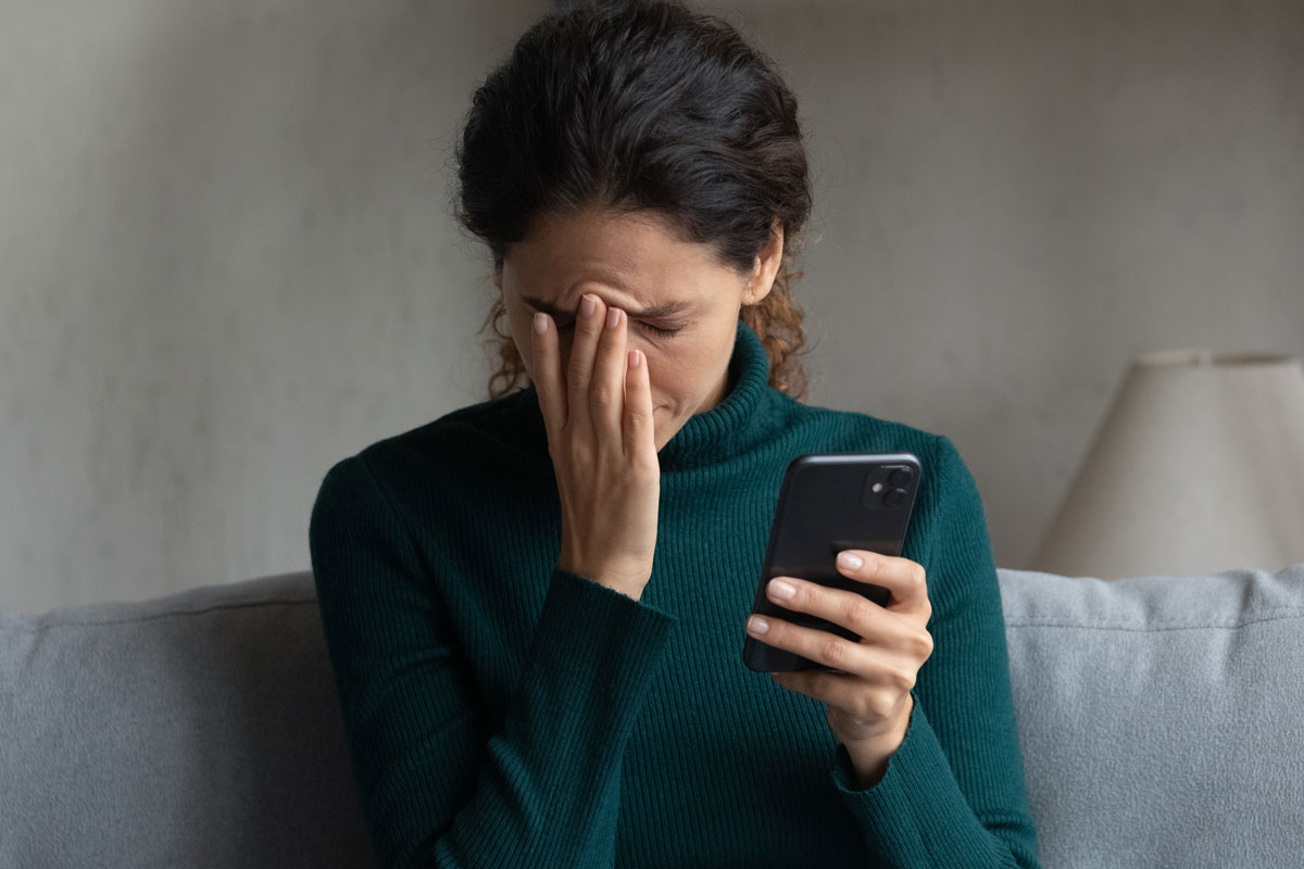 Bad,News,On,Screen.,Confused,Frustrated,Young,Latin,Lady,Cover Braunhaarige Frau mit Petrolfarbenem Rollkragenpullover sind auf einem Sofa. Sie hält ein Smartphone in der Hand und fasst sich mit der anderen verzweifelt an die Stirn.