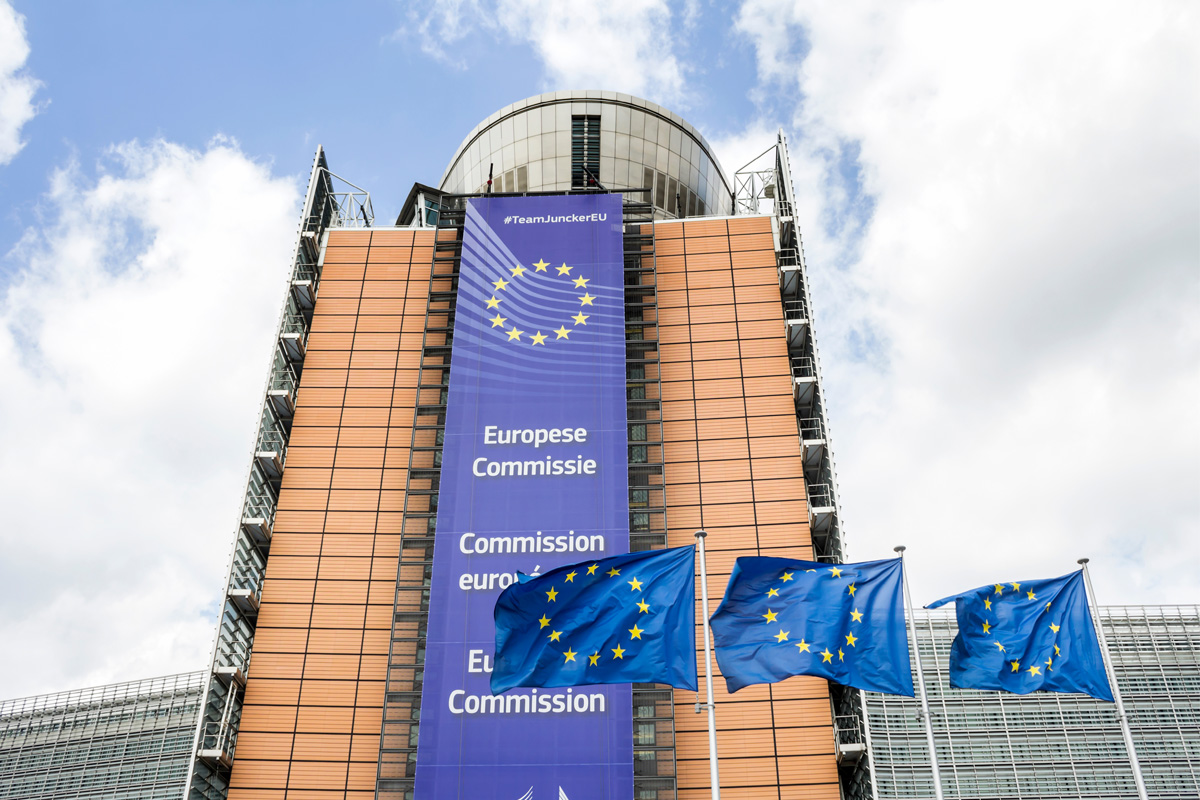 europäische-komission-gebäude-artikelbild-c-shutterstock Foto vom Gebäude der Europäischen Kommission mit drei EU-Flaggen im Vordergrund.