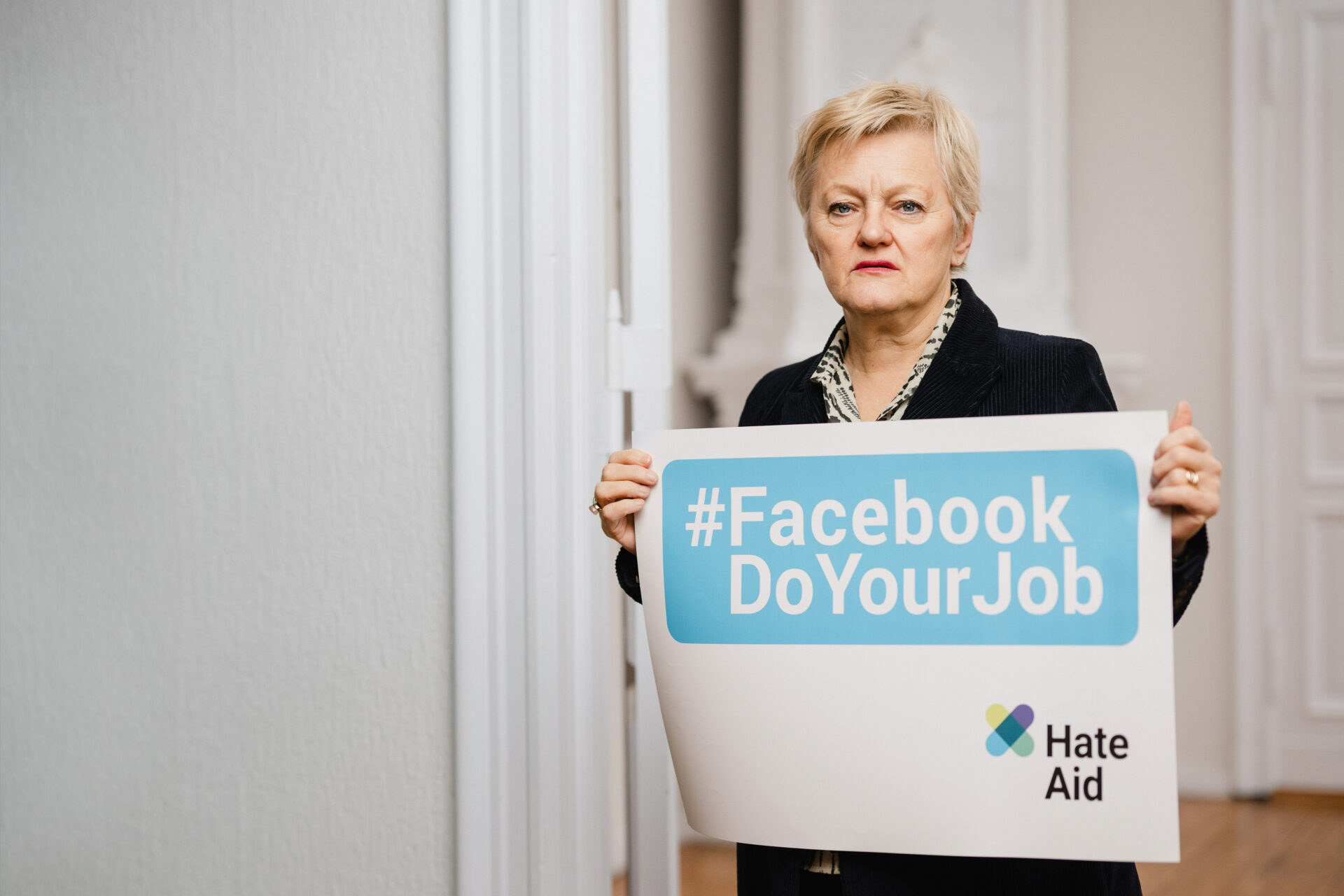 Renate Künast mit #FacebookDoYourJob-Schild. Renate Künast, Bundestagsabgeordnete und HateAid-Klientin, setzt sich mit uns vor dem Bundesgerichtshof in Karlsruhe für die Rechte aller Nutzenden ein.