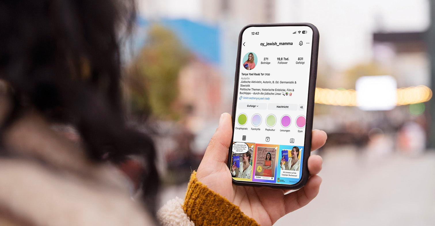 Eine Frau schaut auf ihr Smartphone. Darauf ist der Account von Tanya Yael Raab auf Instagram abgebildet.