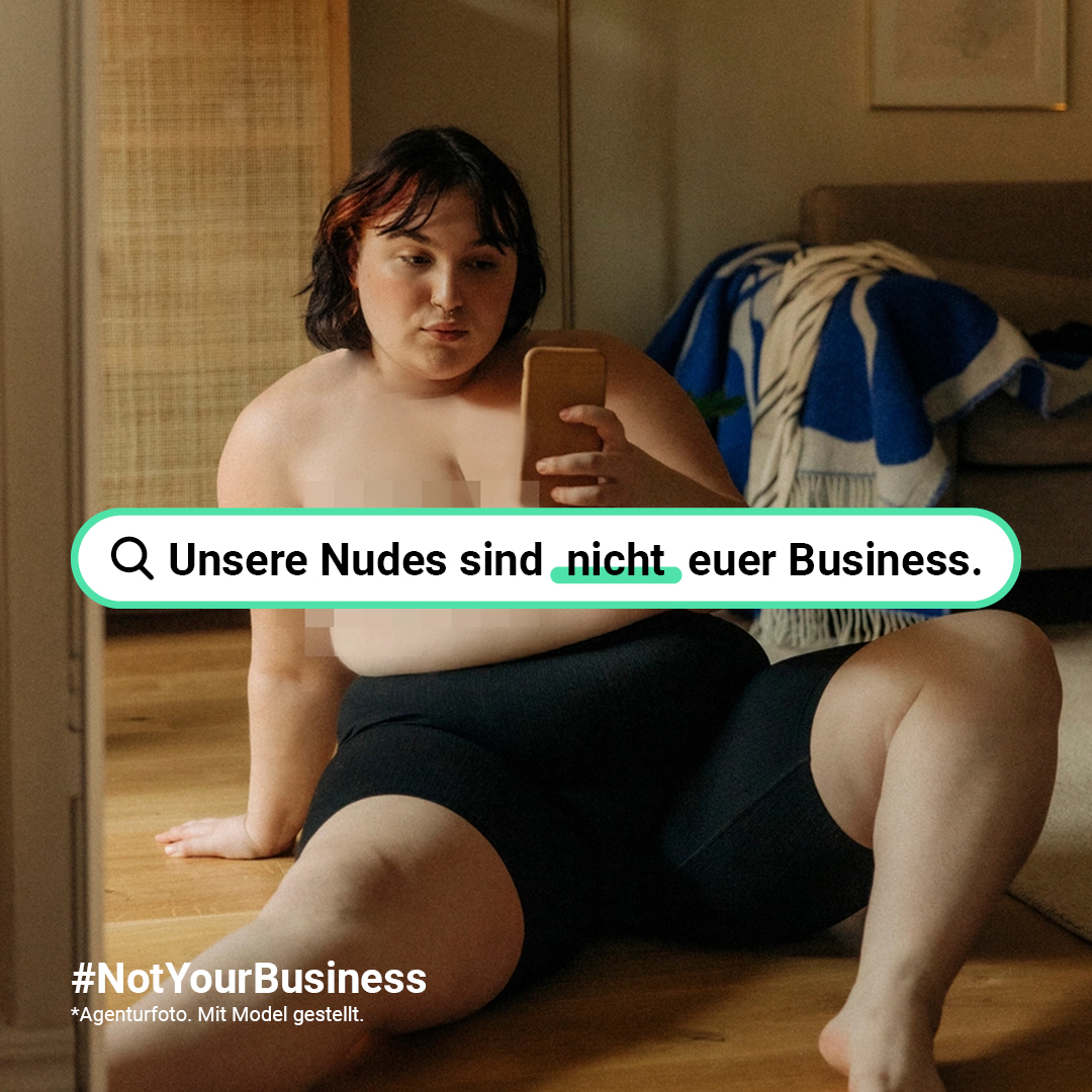 Weiße Frau sitzt ohne Oberteil auf dem Boden und macht mit ihrem Handy ein Selfie vor einem Spiegel. Über ihrem Oberkörper ist eine Suchleiste in der steht: Unsere Nudes sind nicht euer Business.