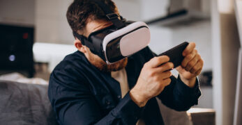 Zu sehen ist ein Mann auf der Couch, der per VR-Brille mit seinem Smartphone interagiert. Copyright: Magnific